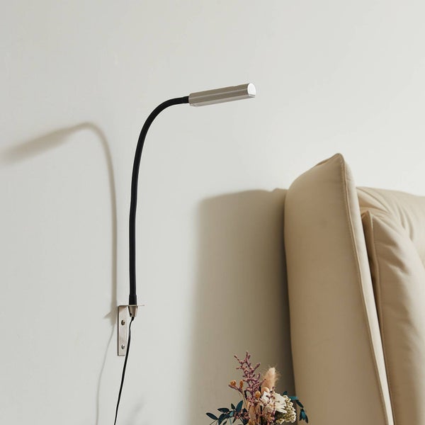 Wandmontierte flexible Leselampe mit schwarzem Schwanenhals und silbernem Kopf neben einem Polsterbett.