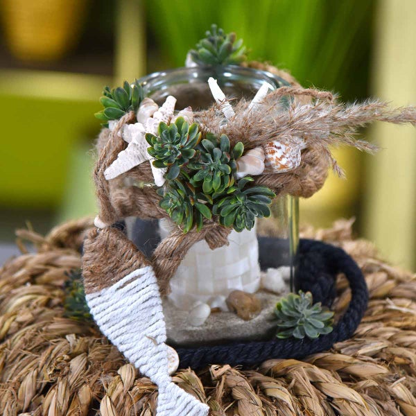 Dekoration mit Sukkulenten, Seesternen, Muscheln und einem Fisch aus Seil in einem Glasgefäß.