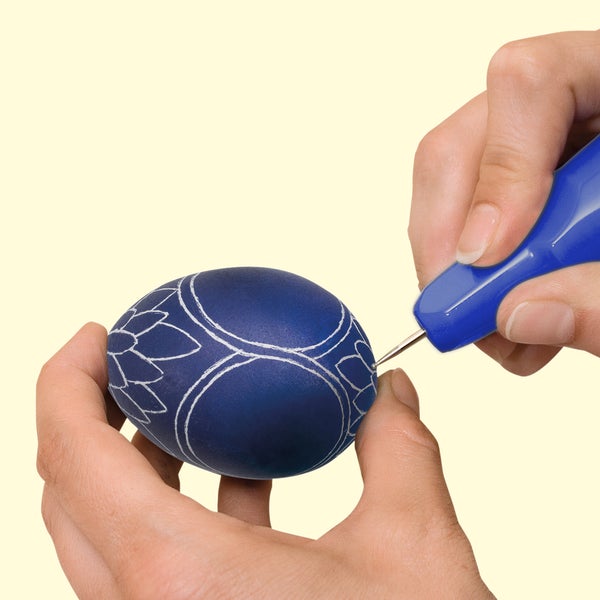 Eine Hand nutzt einen Gravierstift zum Verzieren eines Ostereis mit floralen Mustern.