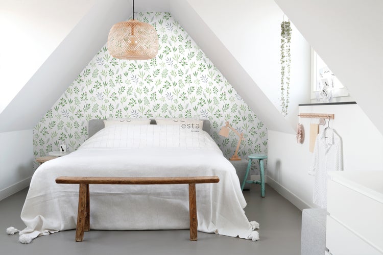 Ein Schlafzimmer im Dachgeschoss mit einem Bett, einem Holzhocker und einer Tapete mit Blattmuster