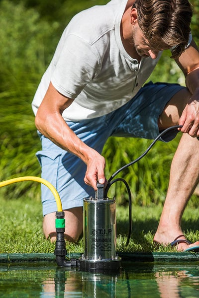 Ein Mann bedient eine T.I.P. Drain 6000/36 Klarwasser-Tauchpumpe aus Edelstahl an einem Gartenteich.