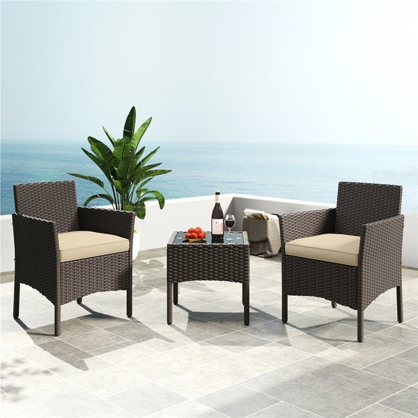 Gartenmöbel-Set mit zwei Korbstühlen, einem Tisch mit Glasplatte und beigen Sitzkissen auf einer Terrasse