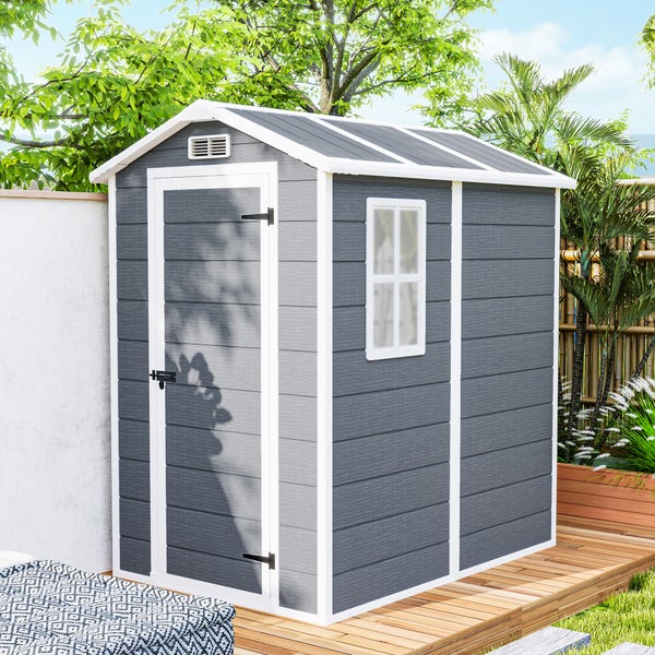 Graues Kunststoff-Gerätehaus mit weißem Satteldach, einer Tür und einem Seitenfenster auf einer Holzterrasse im Garten.
