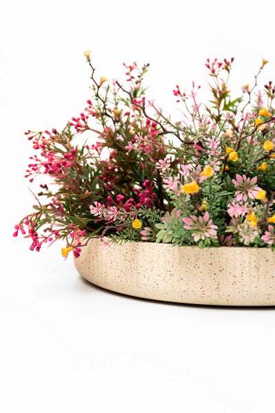 Künstliches Blumengesteck in einer gesprenkelten Keramikschale mit rosa und gelben Blüten.