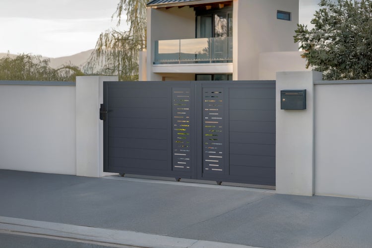 Zweiflügeliges Einfahrtstor aus Metall mit horizontalen Lamellen und dekorativen Lochblech-Elementen vor einem modernen Wohnhaus.