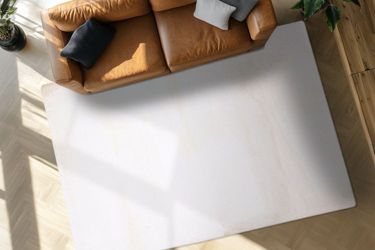 Ein heller rechteckiger Teppich vor einem Sofa auf einem hellen Parkettboden in einem modern eingerichteten Wohnzimmer.