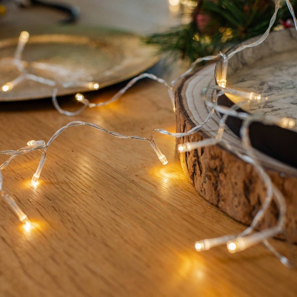 LED-Lichterkette auf einem Holztisch neben einer Holzscheibe und Tannenzweigen.