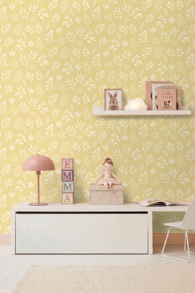 Vliestapete mit weißem Blättermuster auf gelbem Hintergrund in einem hellen Kinderzimmer mit weißen Möbeln und Dekoration.