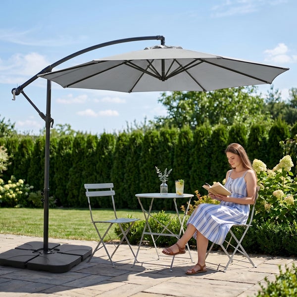 Großer grauer Ampelschirm über einer Sitzgruppe auf einer gepflasterten Terrasse in einem hellen, gepflegten Garten.