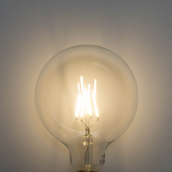 Eingeschaltetes LED Leuchtmittel Globe Form aus klarem Glas mit sichtbaren Filamenten.