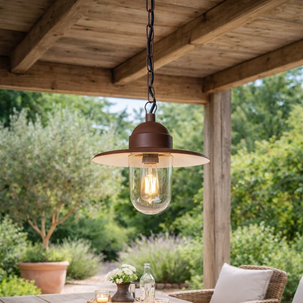 Rustikale Außenpendelleuchte aus Metall mit Glasgehäuse und Edison-Glühbirne an einer Holzdecke über einem Tisch im Garten.