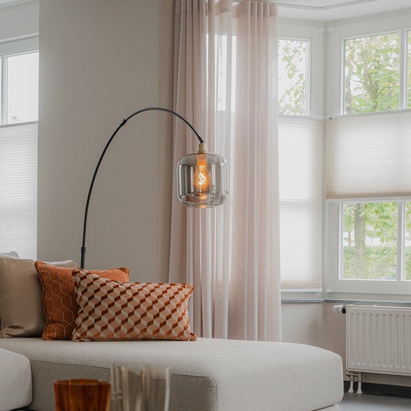 Wohnzimmer mit Bogenlampe, Sofa und Fenstern mit Plissees