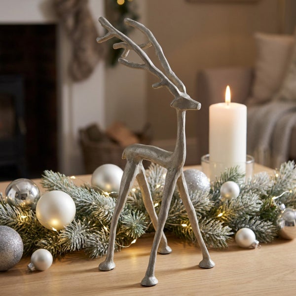 Dekorative Weihnachtsfigur in Form eines Rentiers aus Metall als Tischdekoration umgeben von Tannengrün und Weihnachtskugeln