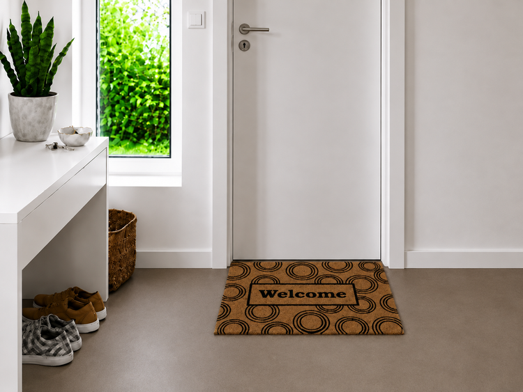 Fußmatte mit Welcome Schriftzug und Kreis Muster vor einer weißen Zimmertür in einem modern eingerichteten Flur mit Konsole und Zimmerpflanze.