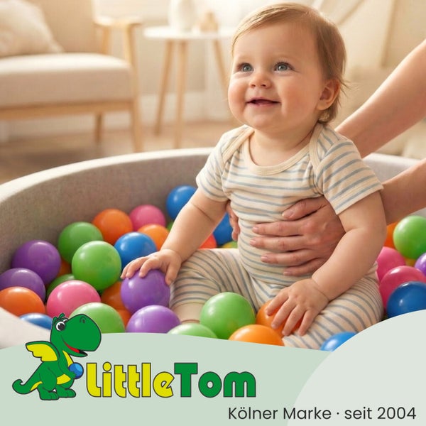 Ein Baby sitzt in einem Bällebad mit bunten Kunststoffbällen, gestützt von Händen. LittleTom Logo.