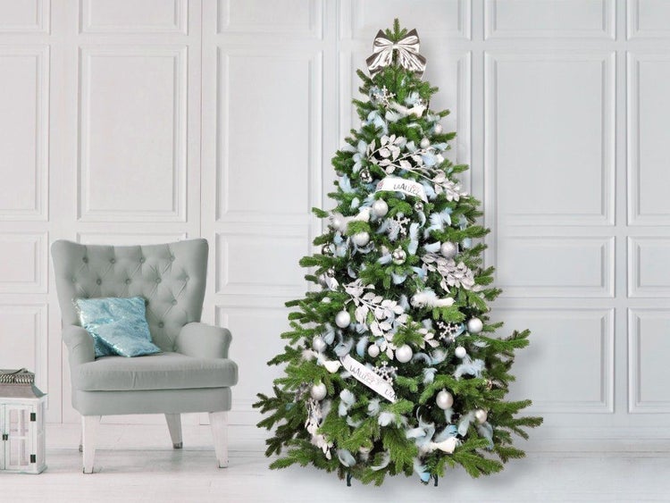Geschmückter Weihnachtsbaum mit silbernen Kugeln, Schleifen und dekorativen Elementen neben einem Sessel in einem weihnachtlich dekorierten Raum.