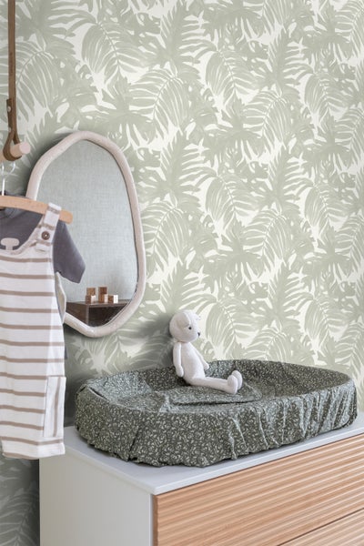 Ein Kinderzimmer mit einer Wickelkommode, einem Spiegel und einer Tapete mit Pflanzenmuster.