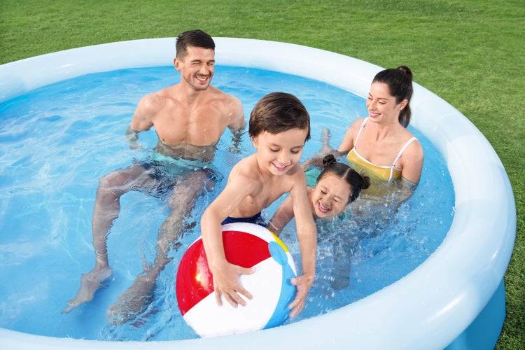 Familie spielt mit Wasserball in einem runden, aufblasbaren Planschbecken auf dem Rasen im Garten.