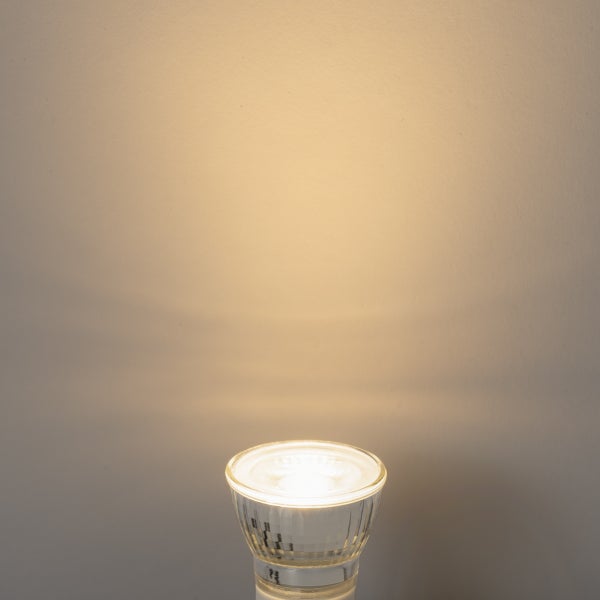 Eingeschaltetes GU10 LED-Leuchtmittel mit warmweißem Lichtkegel an einer Wand.