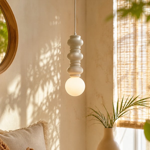 Moderne Pendelleuchte mit skulpturalem Design in einem hellen Wohnraum mit Spiegel und Pflanze.