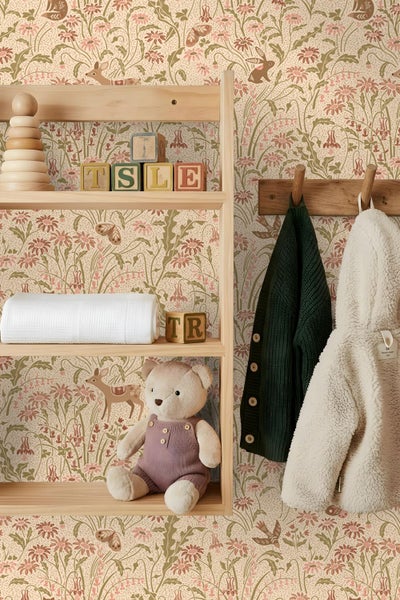 Vliestapete mit floralem Muster und Waldtieren wie Rehen und Hasen in einem hellen Kinderzimmer mit Holzregal und Kinderspielzeug.