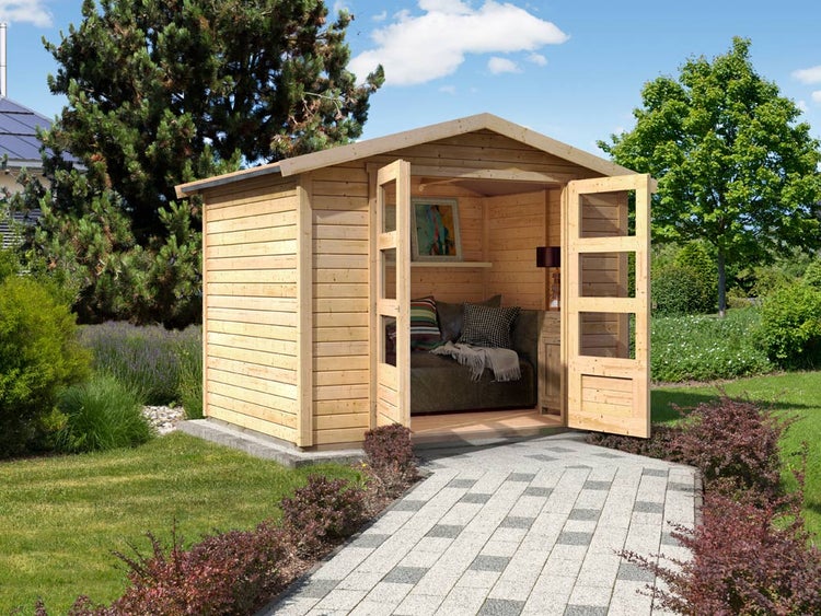 Gartenhaus aus hellem Holz mit geöffneten Doppeltüren und Verglasung, eingerichtet mit Sofa, in einem Garten mit gepflastertem Weg.
