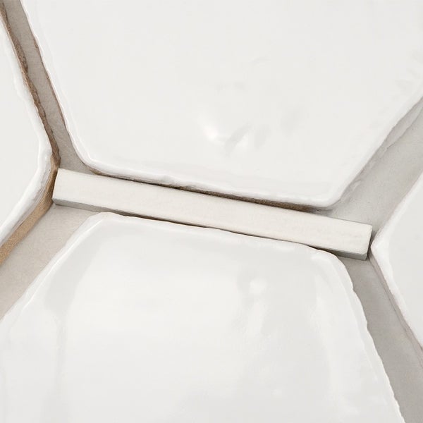 Weiße Wandfliesen in hexagonaler Form mit glänzender Oberfläche und Fugenkreuz bei der Verlegung.