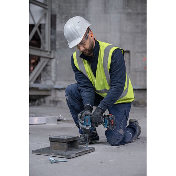 Ein Bauarbeiter befestigt mit einem Akku-Schlagschrauber eine Schraube an einer Stahlplatte.