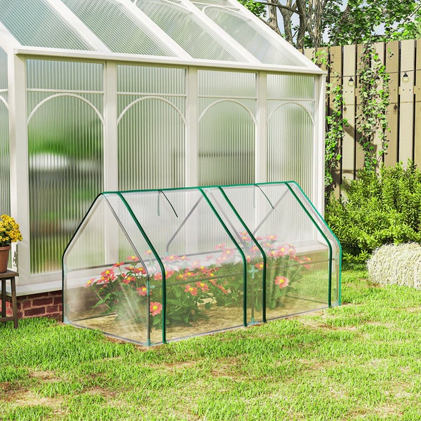Helles Garten-Szenario mit einem kompakten Folien-Gewächshaus auf einer Rasenfläche vor einem großen Gewächshaus.