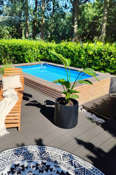Kleiner Pool mit Holzverkleidung auf einer Terrasse mit Holzdeck, Sonnenliege und großem Pflanzkübel im Garten.