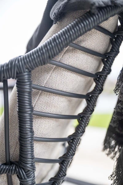 Detailaufnahme eines Gartenstuhls mit schwarzem Metallgestell, schwarzem Seilgeflecht und hellgrauem Stoffkissen.