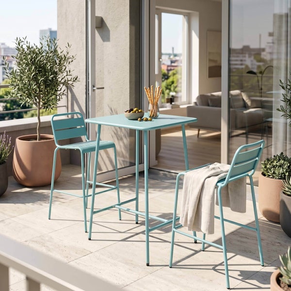 Quadratischer Bartisch und zwei Barstühle aus Metall auf einem modernen Balkon mit Steinboden, Topfpflanzen und Stadtblick.