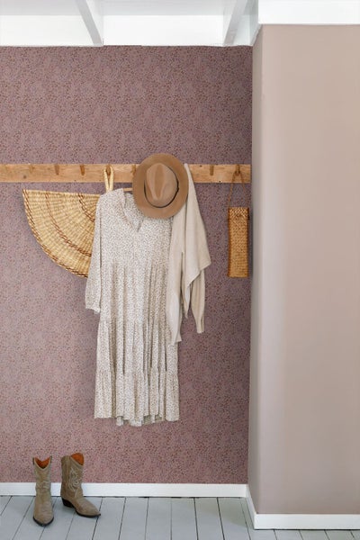 Vliestapete mit floralem Muster an einer Wand, kombiniert mit einer hölzernen Hakenleiste, Kleidung und dekorativen Accessoires.