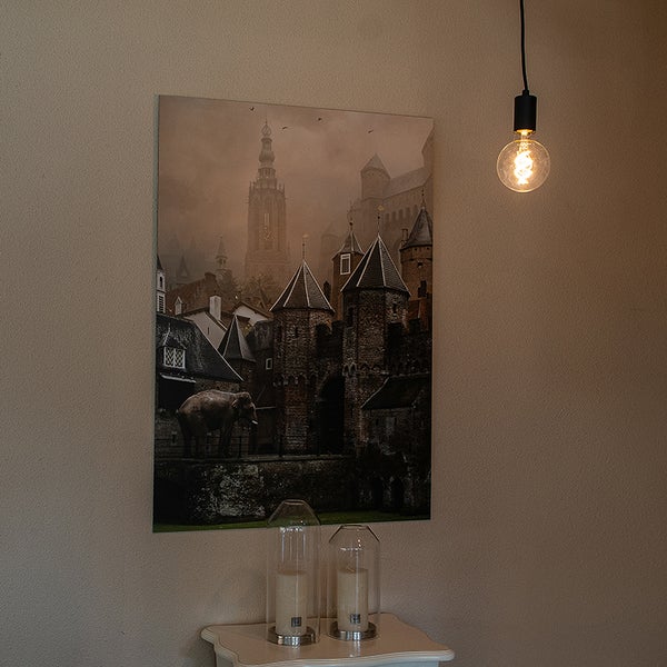 Wandbild mit historischer Stadt und Elefant, davor zwei Glas-Windlichter auf einem Tischchen und eine hängende LED-Globelampe.
