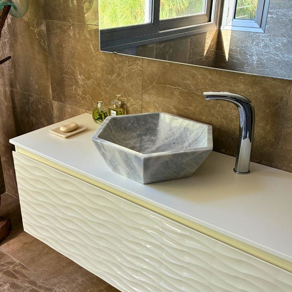 Modernes Badezimmer mit hexagonalem Aufsatzwaschbecken aus grauem Stein, weißem Unterschrank mit Wellenstruktur und verchromter Armatur.