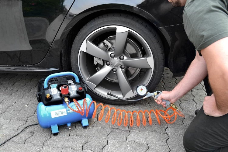 Tragbarer Güde Kompressor mit orangefarbenem Spiralschlauch beim Aufpumpen eines Autoreifens mit einem Reifenfüllmesser.