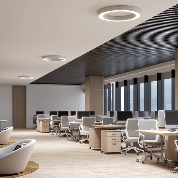 Modernes, helles Großraumbüro mit runden LED-Deckenleuchten, Holztischen und ergonomischen Bürostühlen.