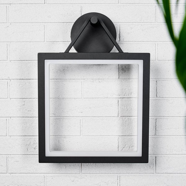 Quadratische schwarze Wandleuchte mit LED-Beleuchtung an einer hellen Ziegelwand.