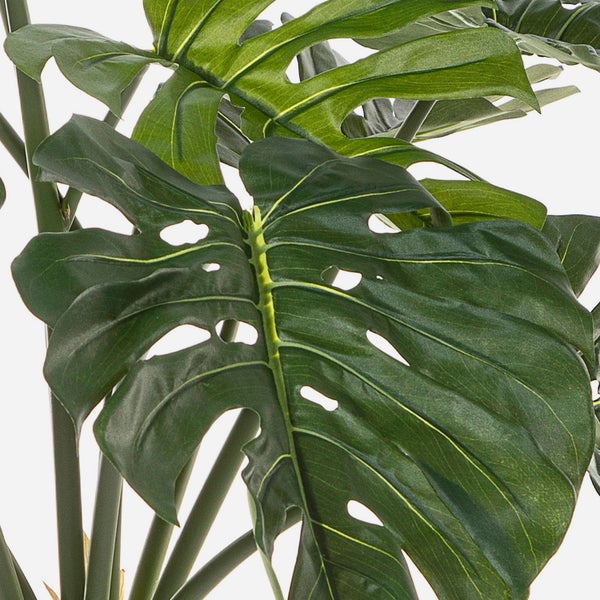 Nahaufnahme eines großen grünen Blattes einer Monstera Kunstpflanze mit charakteristischen Löchern und Blattadern.