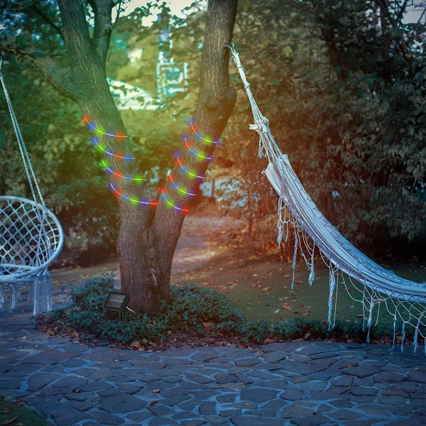 Solar-LED-Lichterkette mehrfarbig um einen Baum gewickelt in einem Garten mit Hängematte und Hängesessel.