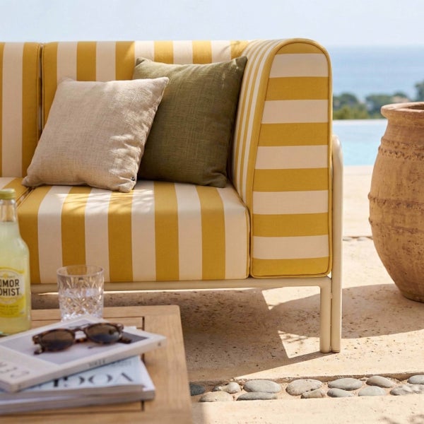 Helles gelb-weiß gestreiftes Gartensofa mit Kissen auf einer Steinterrasse am Pool mit Holztisch und einem Terrakottatopf.