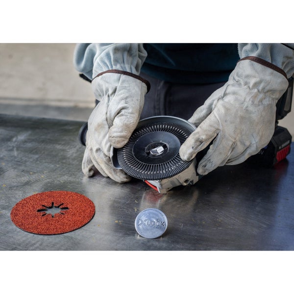 Eine Schleifscheibe mit X-Lock Aufnahme wird von zwei behandschuhten Händen gehalten.