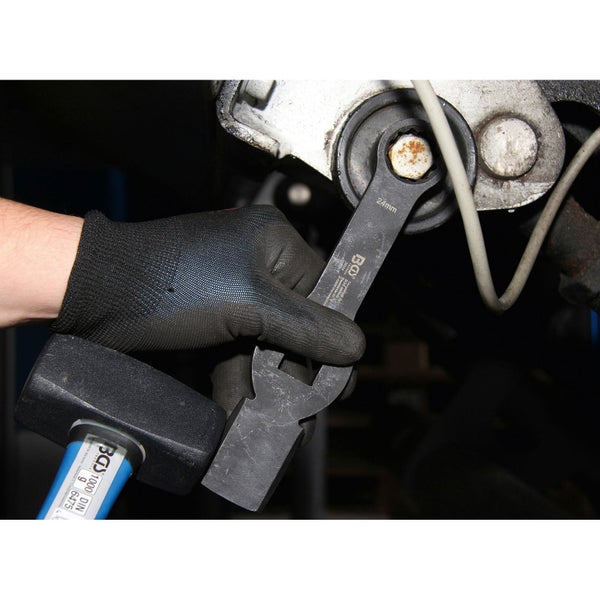 Ein Mann benutzt einen Maulschlüssel der Größe 24 mm an einem Maschinenteil, während ein Hammer daneben liegt