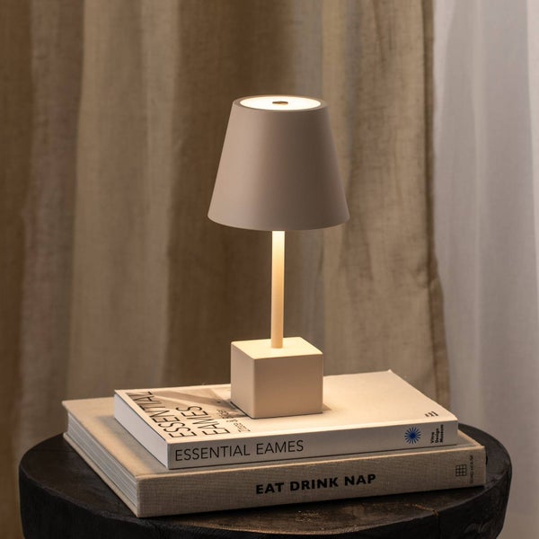 Kleine kabellose LED Tischleuchte mit konischem Schirm und quadratischem Sockel auf Büchern vor einem Vorhang stehend