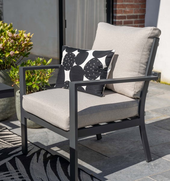 Moderner Gartenstuhl aus Metall mit hellgrauen Polstern und gemustertem Zierkissen auf einer sonnigen Terrasse.