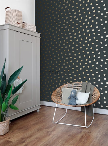 Ein Kinderzimmer mit einer dunkel gemusterten Tapete, einem Kleiderschrank und einem Rattansessel.
