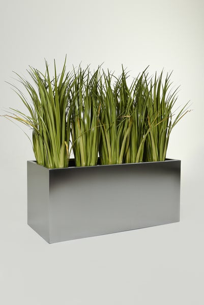 Künstliches Gras in einem rechteckigen, silbernen Pflanzkasten aus Metall.