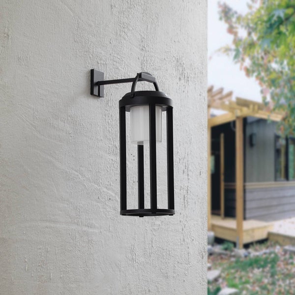 Moderne schwarze Außenwandleuchte mit weißem Zylinderglas an einer hellen strukturierten Hausfassade.