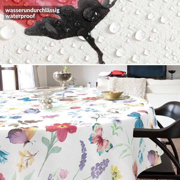 Runde Tischdecke mit bunten Blumen und Schmetterlingen auf weißem Grund, wasserundurchlässiges Material mit Wassertropfen im Detail.
