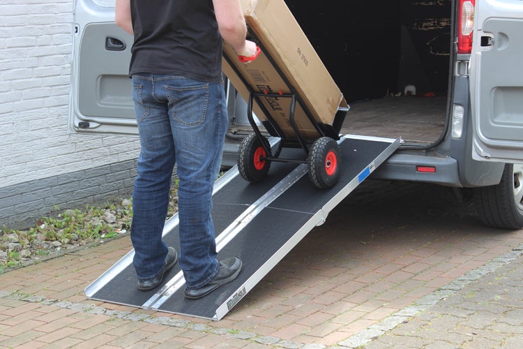 Eine Person schiebt mit einer Sackkarre eine Kiste über eine Rampe in einen Transporter.